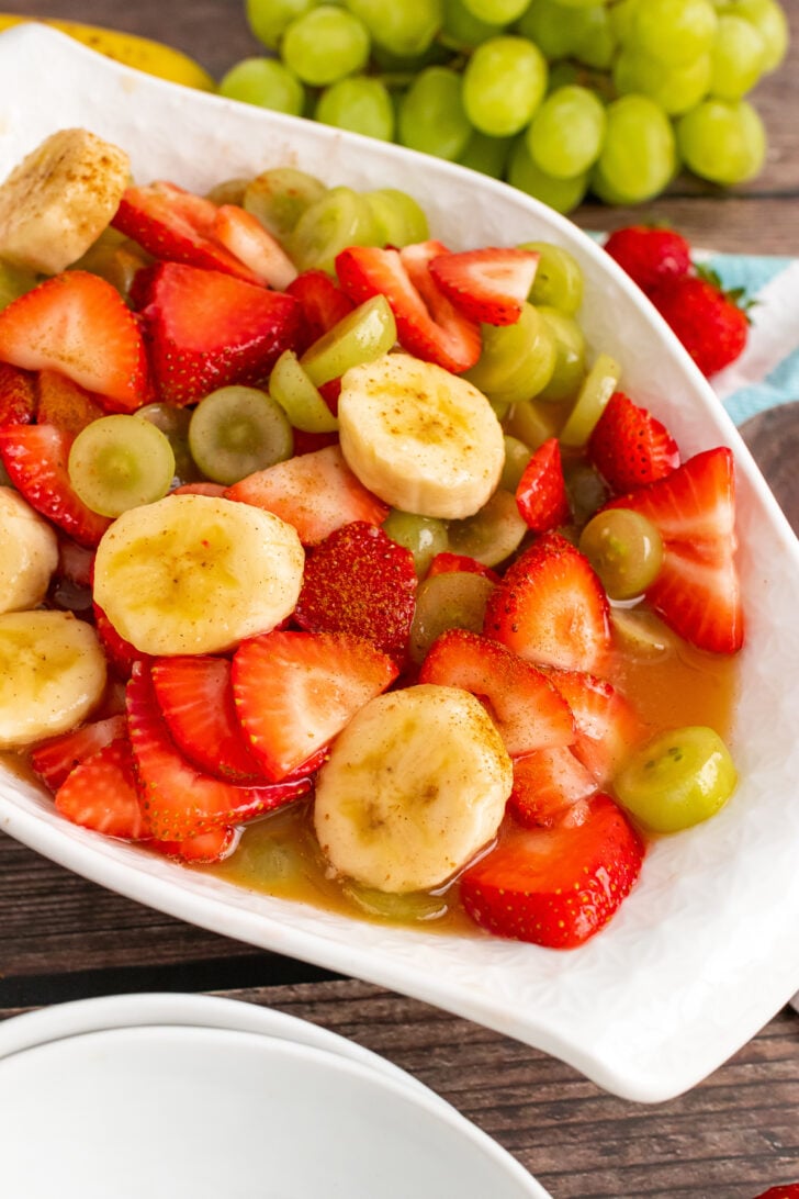 Strawberroes, bananas and green grapes in a dressing served in a white oblong bowl.