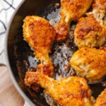 Crispy golden ovenfried chicken drumsticks and thighs in a cast iron skillet on a wooden surface