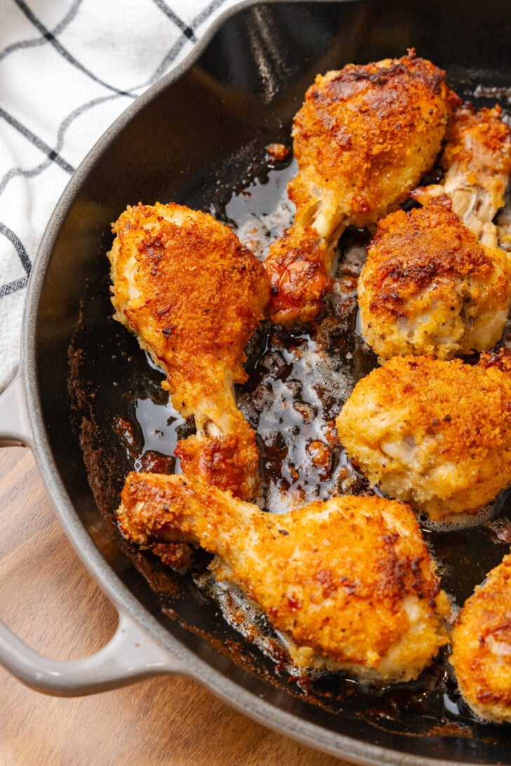 Crispy golden ovenfried chicken drumsticks and thighs in a cast iron skillet on a wooden surface