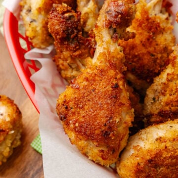 Fried chicken leg served on white parchment paper in a red basket.