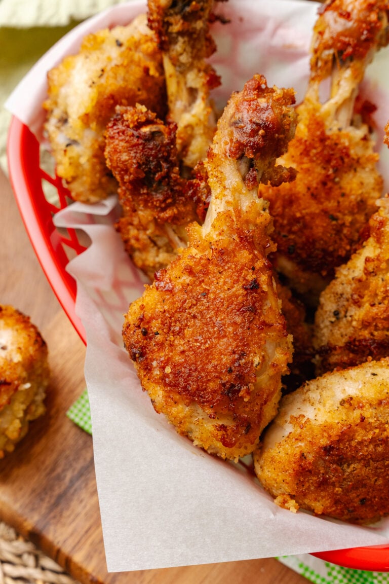 Fried chicken leg served on white parchment paper in a red basket.