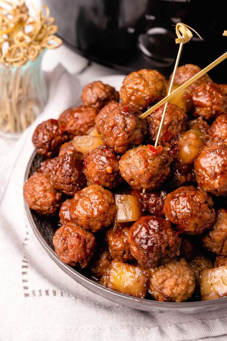 Cooked meatballs with pineapple chunks in a bowl served with wooden skewers.