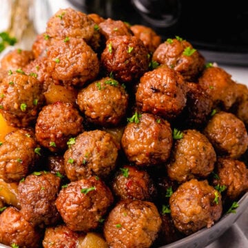 Cooked meatballs with pineapple chunks in a bowl served with wooden skewers.