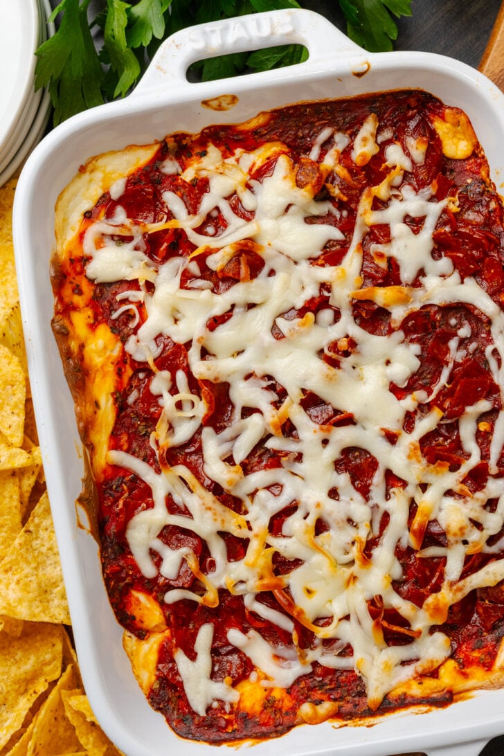White casserole dish with baked pepperoni dip topped with cheese and served with tortilla chips.
