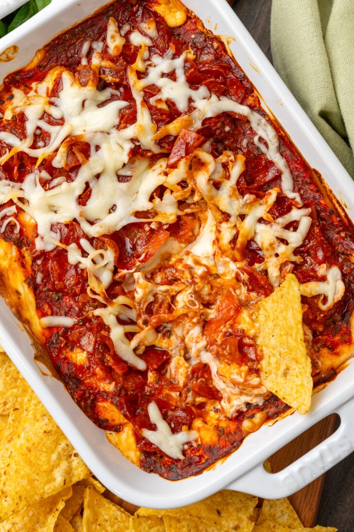 White casserole dish with baked Pepperoni Dip with 1 tortilla chip.