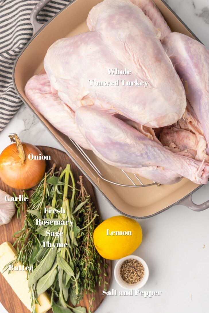 Raw turkey in a roasting pan, onion, garlic bulb, butter, lemon, salt, pepper, fresh rosemary, thyme and sage labeled with white text.