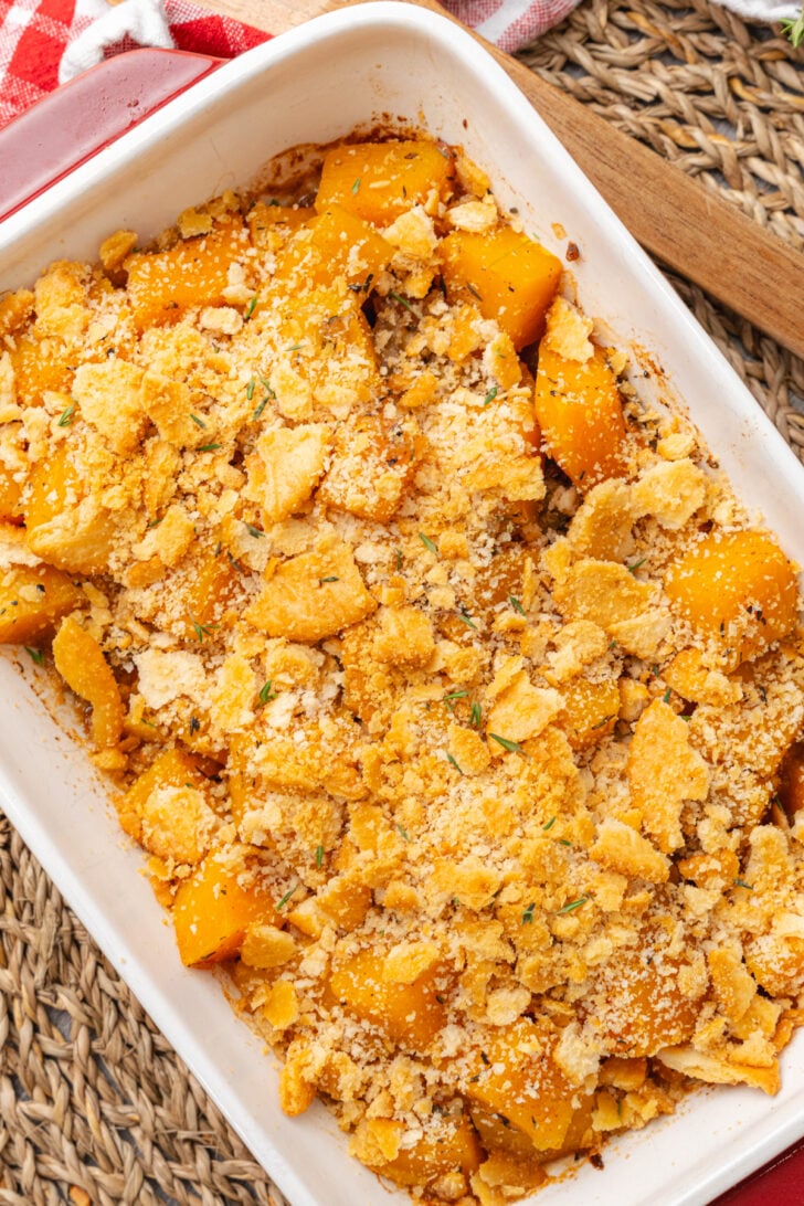 Brown butter butternut squash topped with crackers and baked in a white rectangle baking dish resting on a woven mat.
