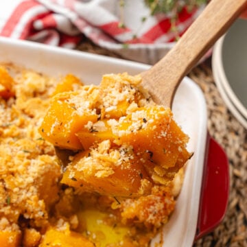 Brown butter butternut squash topped with crackers and baked in a white rectangle baking dish served with a wooden spoon.