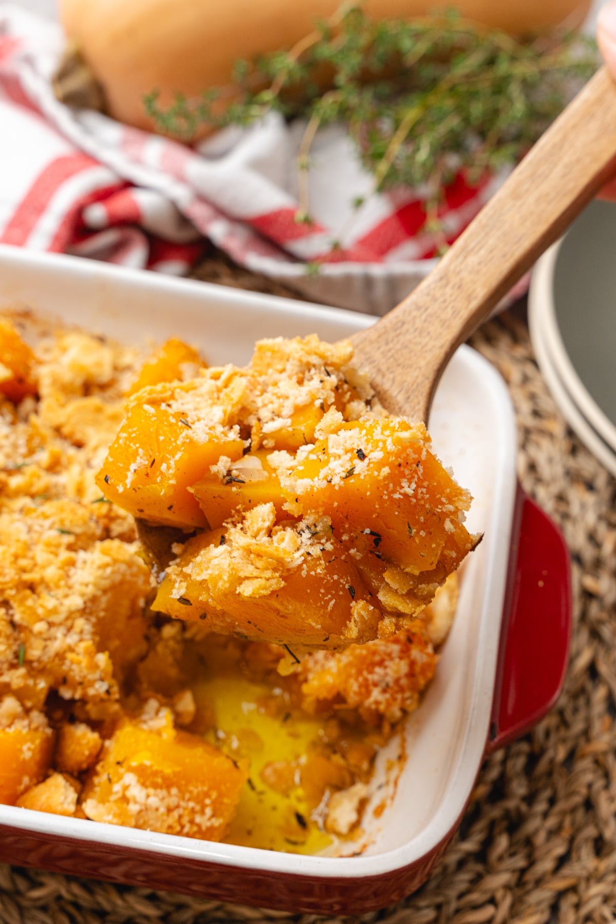 Brown butter butternut squash topped with crackers and baked in a white rectangle baking dish served with a wooden spoon.