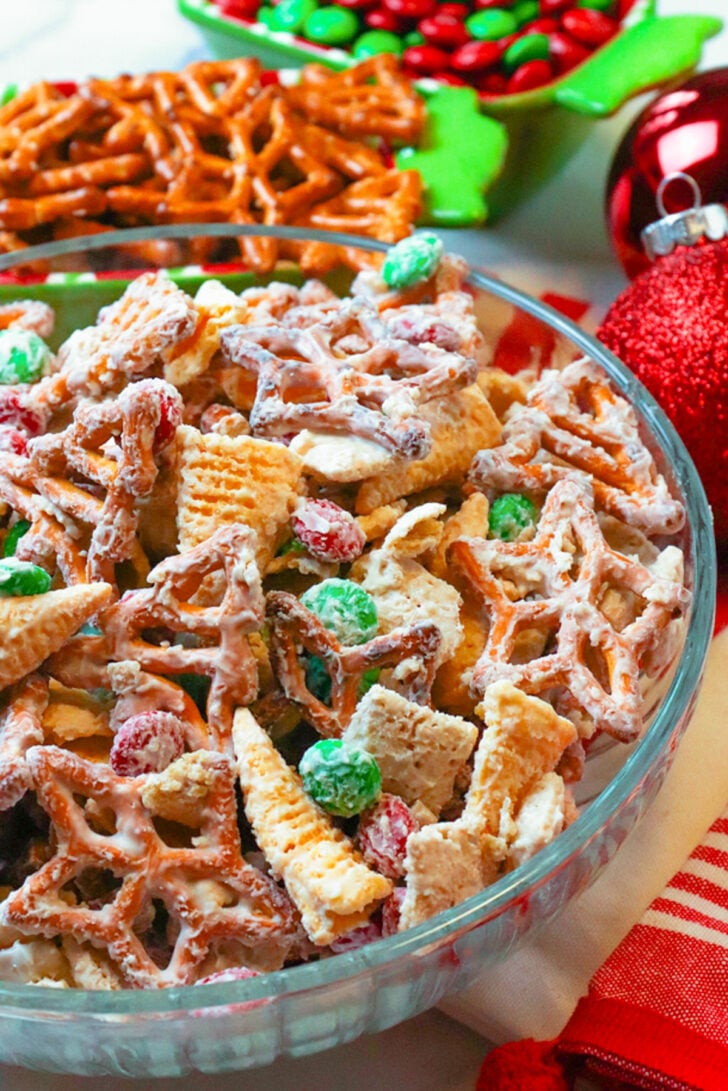Glass bowl with pretzels, bugel chips and chocolate candies coated in vanilla for Christmas snack mix with star shaped pretzels and M&Ms.