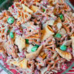 Glass bowl with pretzels, bugle chips and chocolate candies coated in vanilla for Christmas snack mix.