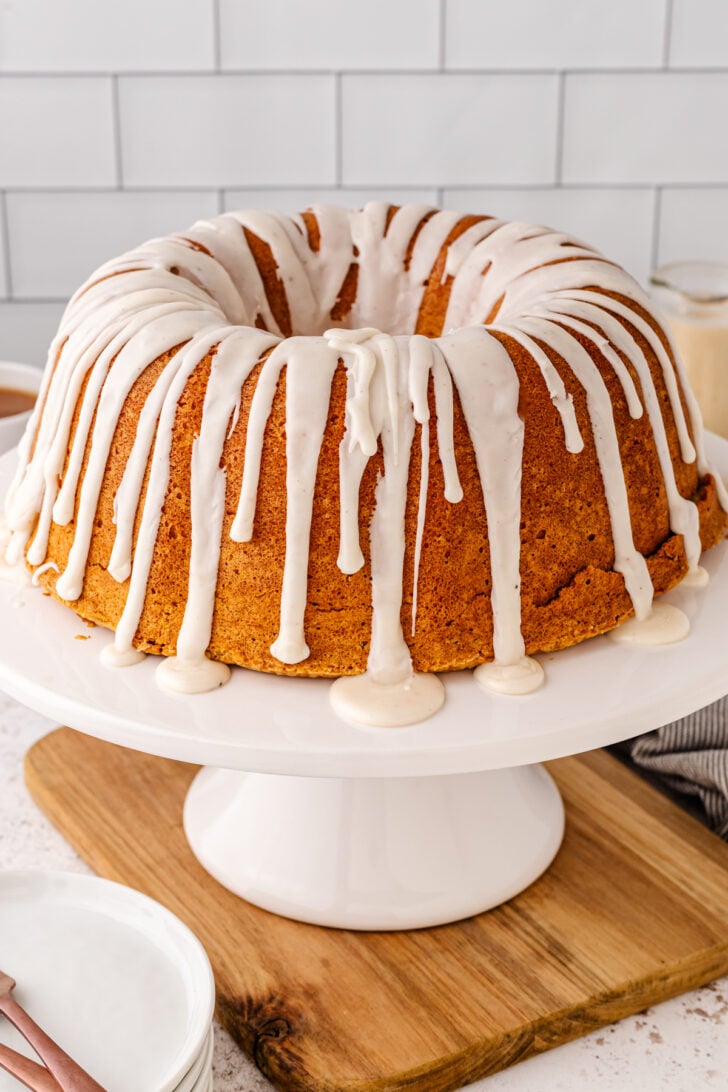 Eggnog Pound Cake with a white icing drizzle served on a white cake stand resting on a wooden board.