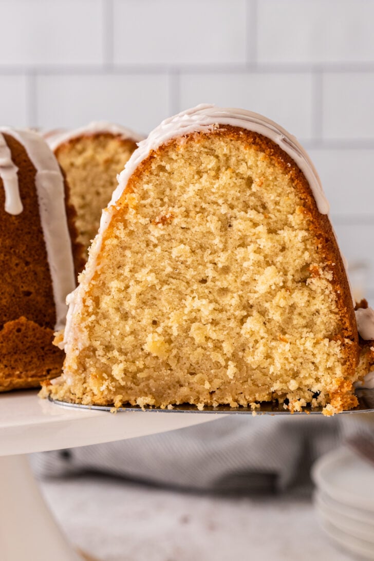 Slice of eggnog pound cake cut and served from a white cake stand with a metal spatula.
