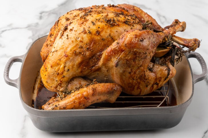 Whole roasted turkey garnished with fresh herbs and lemon slices in a roasting pan.
