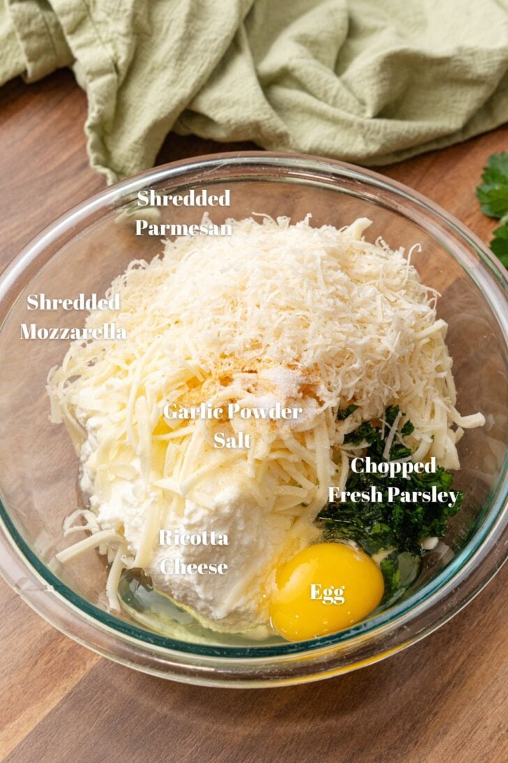 Glass bowl with ricotta cheese, mozzarella, and Parmesan, egg, chopped fresh parsley, garlic powder and salt.
