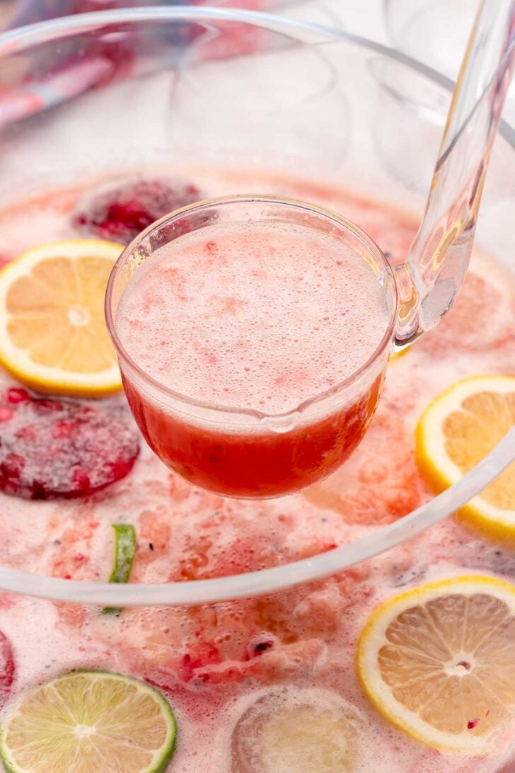 Ladle full of berry sherbert punch served with. lemon and lime slices.
