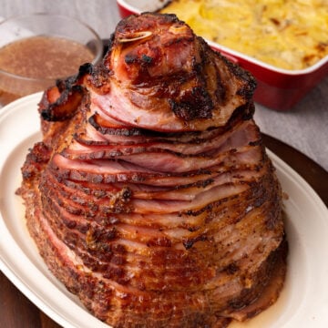 Glazed brown sugar mustard ham sliced on white plate with cornbread casserole and gravy in background