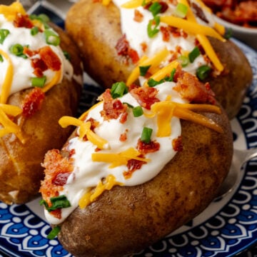 Baked potatoes topped with sour cream cheese bacon bits and chives ontop of a nice blue plate.