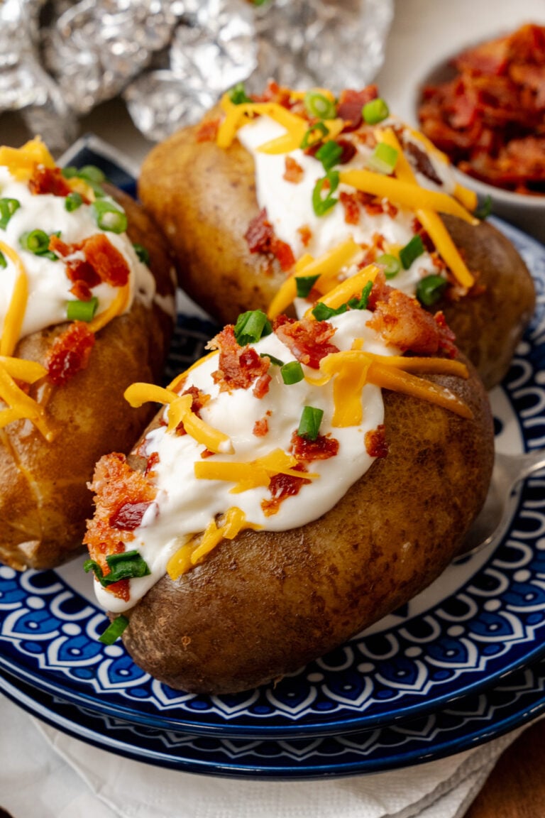 Baked potatoes topped with sour cream cheese bacon bits and chives ontop of a nice blue plate.