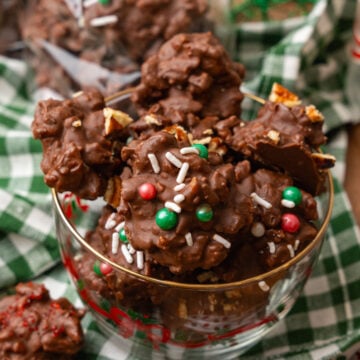Chocolate pecan candy with green and red candy and white sprinkles and chopped pecans in a glass Christmas bowl.