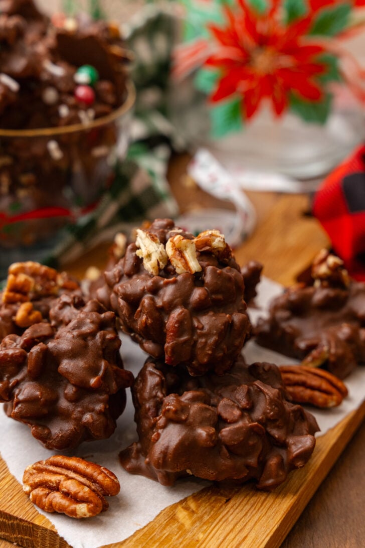 Chocolate pecan candy with chopped pecans on parchment paper resting on a wooden board with pecan halves.