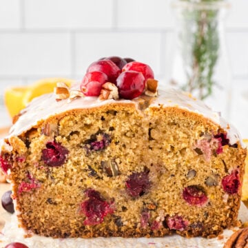 Slice of cranberry orange quick bread with pecans on a metal cooling rack, topped with fresh cranberries.