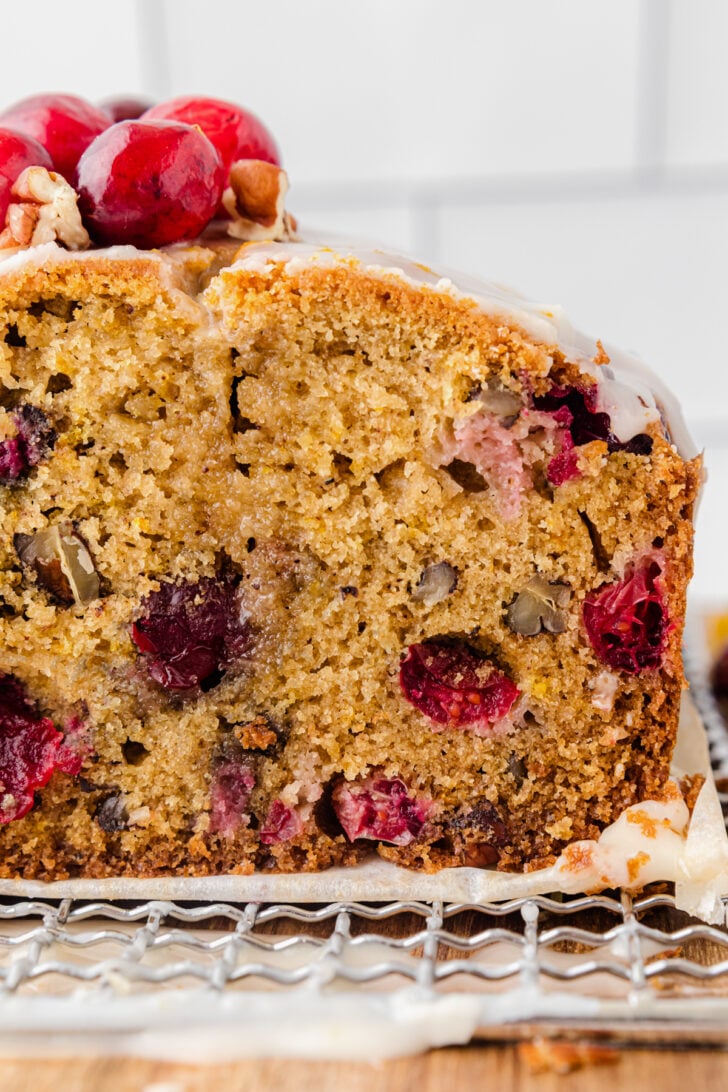 Slice of cranberry orange quick bread with pecans on a metal cooling rack, topped with fresh cranberries.