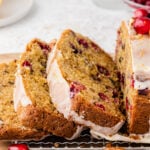 Slices of cranberry orange quick bread on a wire cooling rack garnished with pecans and whole fresh cranberries.