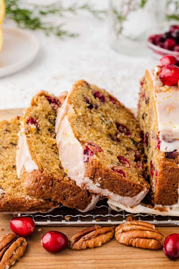 Slices of cranberry orange quick bread on a wire cooling rack garnished with pecans and whole fresh cranberries.
