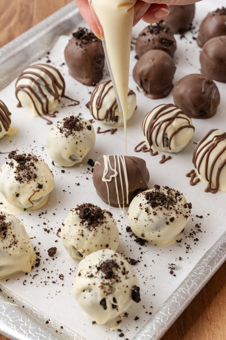 Chocolate Oreo truffles being drizzled with a white chocolate piping on a baking sheet.
