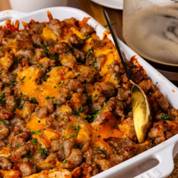 White cast iron baking dish with sausage and cheese croissant casserole topped with chives and served with a gold spoon.
