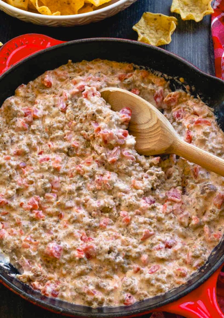 Delicious sausage dip in a cast iron pan with bright red tomatoes and melted cream cheese and tortilla chips on the side ready for dipping.