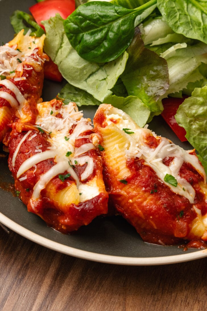 Cooked stuffed shells with cheese and sauce and a side of salad on a plate.