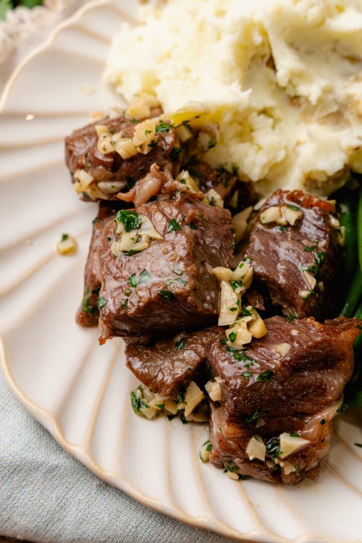 Air Fryer steak bites with garlic and parsley with mashed potatoes on a white plate.