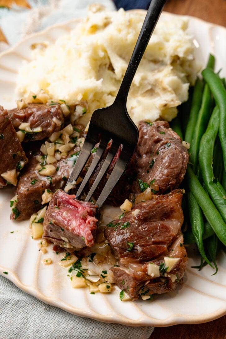 Air Fryer steak bites with garlic and parsley with mashed potatoes and green beans on a white plate.