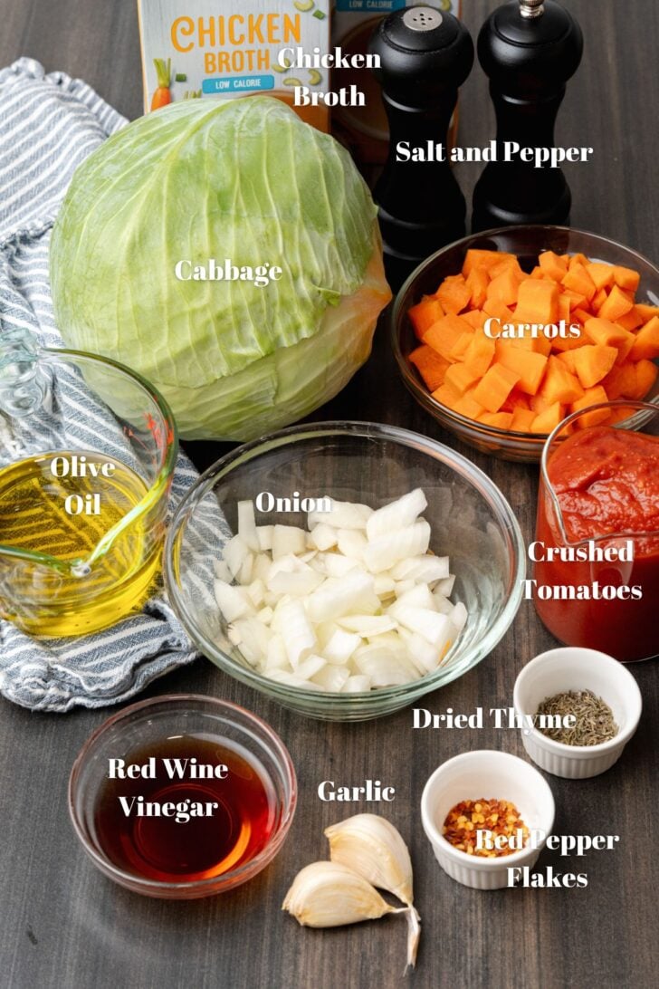 Ingrediets, cabbage, carrots, onions, tomato sauce, salt, pepper, chicken broth, vinegar, garlic and seaoning on a wooden cutting board.