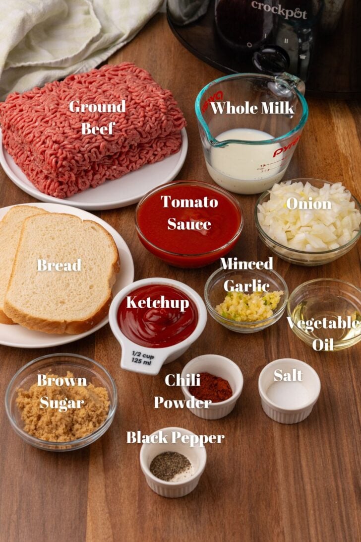 Ingredients needed to make sloppy joes. Ground beef, whole milk, onion, tomato sauce, minced garlic, vegetable oil, salt, pepper, chili powder, brown sugar, ketchup, and bread. All sitting inside nice measuring cups or ramekins.