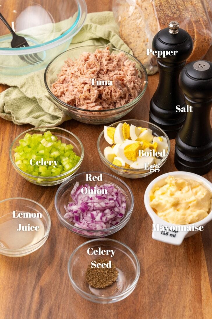 Ingredients for tuna salad on a cutting board. Tuna, salt, pepper. eggs, mayonnaise, red onion, celery, lemon juice and celery seed.