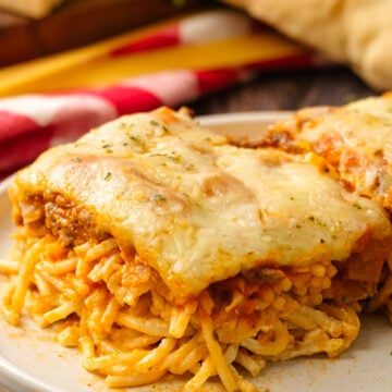 Baked spaghetti cropped 8 with cheese topping on white plate, fresh ingredients and red peppers visible in background