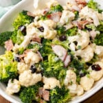 White bowl filled with broccoli cauliflower salad with cooked bacon and dried cranberries.