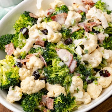 White bowl filled with broccoli cauliflower salad with cooked bacon and dried cranberries.