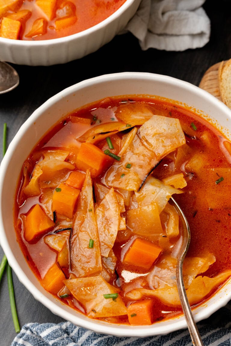 White bowl filled to the top with cozy cabbage soup and a spoon taking some out.