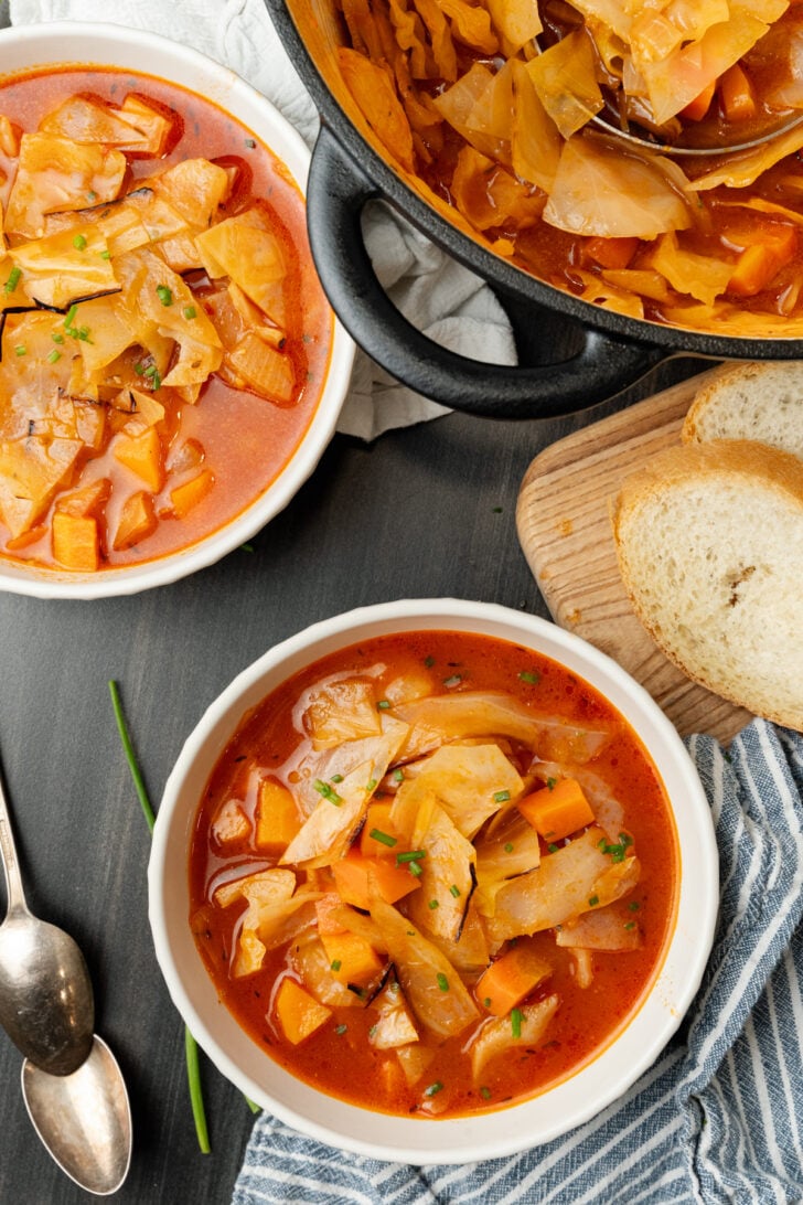 White bowl filled to the top with cozy cabbage soup and a black pot full of it.