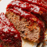 Sliced homemade meatloaf with thick glaze served on a white plate.