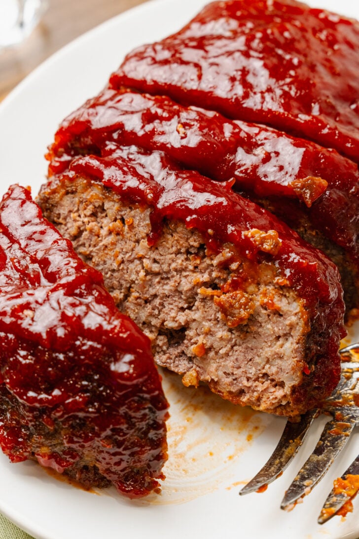 Sliced meatloaf topped with a red, thick glaze served on a white plate.