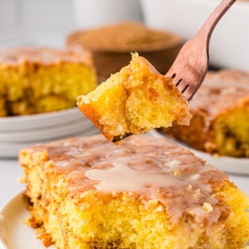 Honey bun cake on a white serving plate. With a chunk of it taken on with a fork ready to eat!