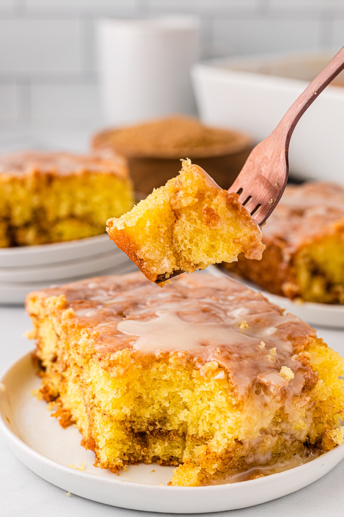 Honey bun cake on a white serving plate. With a chunk of it taken on with a fork ready to eat!