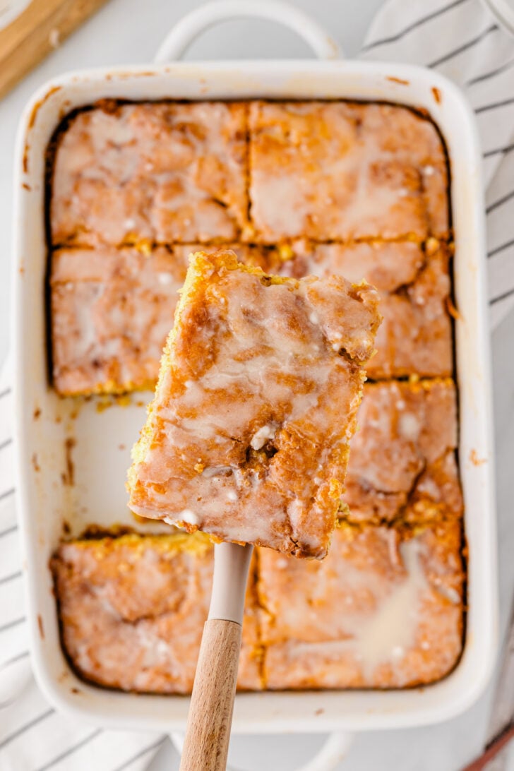 Perfectly baked honey bun cake cut into squares in a white baking dish being lifted up by a spatula.