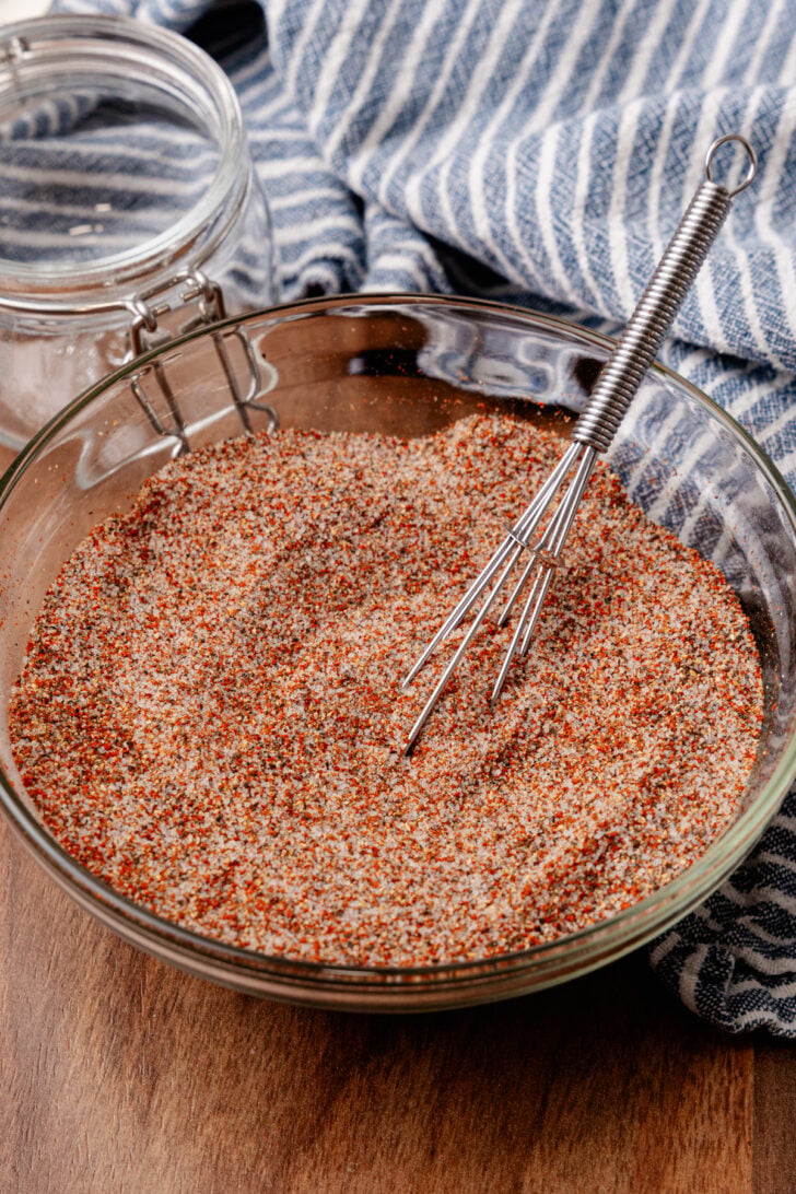 House seasoning blend in a large bowl with a whisk in it placed on top of a cutting board.