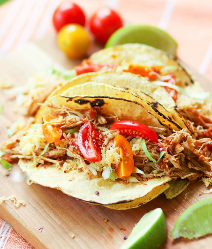 Mexican chicken taco2 with shredded meat, red peppers, and green onions on corn tortillas with lime wedges on wooden board